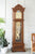 Reloj de pie de madera con mecanismo visible tras cristal y líneas decorativas de péndulo