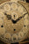 Esfera de reloj de pie con números romanos, adornos de filigrana y mecanismo de manecillas negro.