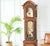 Reloj de pie con caja de madera marrón, vitrina de cristal y péndulo colgante en el interior.