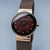 "Reloj de mujer con esfera de color rojo oscuro, índices de bastón y caja en tono oro rosa; correa de malla."