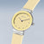 "Reloj de mujer: esfera amarilla, manecillas negras, correa beige, corona plateada"
