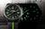 Reloj de hombre con esfera negra y marcadores luminosos verdes, correa de textil negro