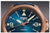 Primer plano de reloj de hombre con esfera azul, índices luminosos y símbolo de automático