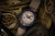 Pulsera de hombre con correa textil beige, bisel negro y esfera beige.