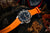 Reloj para hombre con correa de caucho naranja, esfera negra y bisel plateado