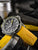 Pulsera de hombre en detalle: correa amarilla, caja plateada, esfera visible