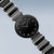 Reloj de mujer con esfera negra y correa de metal, vista lateral oblicua.