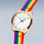 "Reloj de mujer con caja dorada y pulsera textil multicolor, vista lateral"