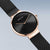 Reloj con esfera negra, manecillas de oro rosa y correa milanesa negra