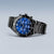 Reloj de hombre con esfera azul, bisel negro y correa ancha de metal, vista lateral