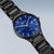 "Reloj de hombre con esfera azul y correa de titanio negra, vista lateral"