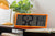 Retro-LCD-Wanduhr in Neonorange auf Tisch mit digitaler Anzeige von Uhrzeit und Datum