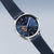Reloj de hombre con esfera redonda azul, mecanismo visible y correa milanesa azul