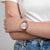 "Reloj de mujer en la muñeca con correa de malla rosa y esfera clara"