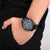 Reloj cronógrafo en la muñeca: esfera azul, caja negra, correa de cuero