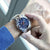 Reloj cronógrafo para hombre en la muñeca: esfera azul con correa de metal plateado.