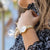 "Reloj de mujer en la muñeca con pulsera dorada y esfera blanca, cuarzo."