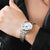 Reloj de mujer en la muñeca, correa de metal plateado y esfera blanca con números negros