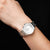 "Reloj de mujer en la muñeca con pulsera de metal plateado y esfera blanca"