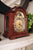 Reloj de mesa de caoba en vista lateral, con péndulo y esfera visibles a través de la abertura