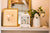 Reloj de mesa blanco sobre alféizar con esfera floral junto a ramo de flores