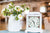 Reloj de mesa blanco con esfera floral junto a flores en jarrón de cerámica