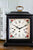 Vista de cerca: reloj de mesa con borde floral, números romanos y puntos dorados