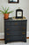 Reloj de mesa sobre cómoda azul oscuro junto a planta en maceta, carcasa negra, esfera floral