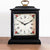 Reloj de mesa negro con frente de cristal, asa dorada y esfera blanca con flores