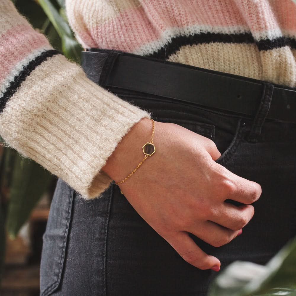 Pulsera dorada con colgante de madera cuadrado en la muñeca
