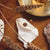 Pulsera sobre tela blanca: cadena dorada con colgante de madera cuadrado