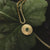 "Collar dorado con colgante redondo y piedra verde, vista frontal"
