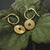 Aros dorados con colgante de sol redondo y piedra verde, llevados en fundas de hojas