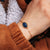 Pulsera de eslabones dorada con colgante ovalado azul en la muñeca