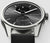 Smartwatch con esfera gris, caja plateada, correa negra y pantalla de temperatura