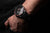 "En la muñeca: reloj para hombre con esfera negra y correa negra perforada"