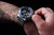 Reloj de hombre en la muñeca con bisel azul, esfera negra y correa de acero inoxidable