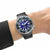 Reloj de hombre en la muñeca con correa de caucho negra, esfera azul e índices luminosos.