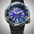 Vista frontal de reloj para hombre con esfera azul-violeta, bisel plateado y correa negra.
