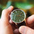 Reloj unisex en mano: esfera verde, correa de cuero marrón y fecha a las 10.