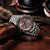 Pulsera de hombre de perfil con correa de acero inoxidable plateado y esfera marrón de cronógrafo.
