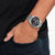 Reloj de pulsera de acero inoxidable en la muñeca con esfera negra y correa de metal plateado