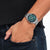 Pulsera de hombre en la muñeca con esfera verde y correa de acero inoxidable plateado.