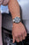 Pulsera de hombre en la muñeca con esfera negra y correa de metal.