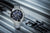 Chronograph-Herrenuhr aus schräger Ansicht: Edelstahlband, schwarzes Zifferblatt