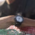 Reloj de buceo Luminox en la muñeca con correa negra y esfera blanca, gotas de agua