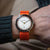 Reloj de hombre en la muñeca con correa textil naranja, esfera redonda blanca