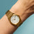 Reloj dorado de mujer con esfera blanca y pulsera de metal dorado en la muñeca