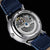 Reloj automático para hombre con vista abierta al mecanismo, correa de cuero azul, caja de acero inoxidable