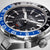 Primer plano de reloj de hombre: esfera negra con índices blancos y manecilla GMT